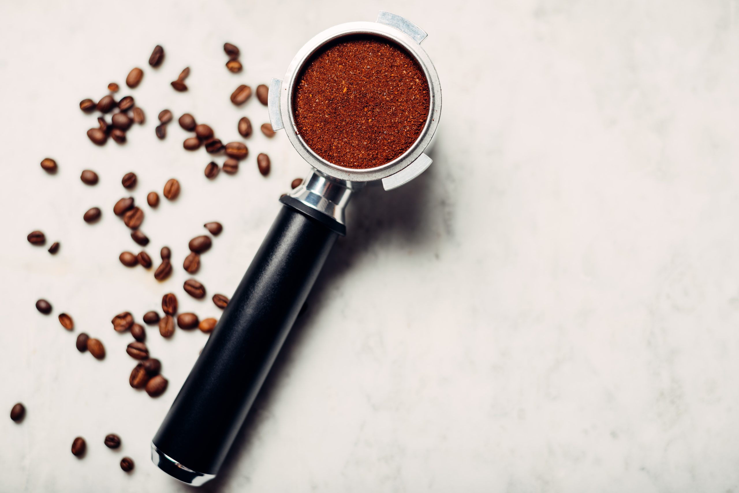 Portafilter filled with fresh ground coffee, surrounded by whole coffee beans